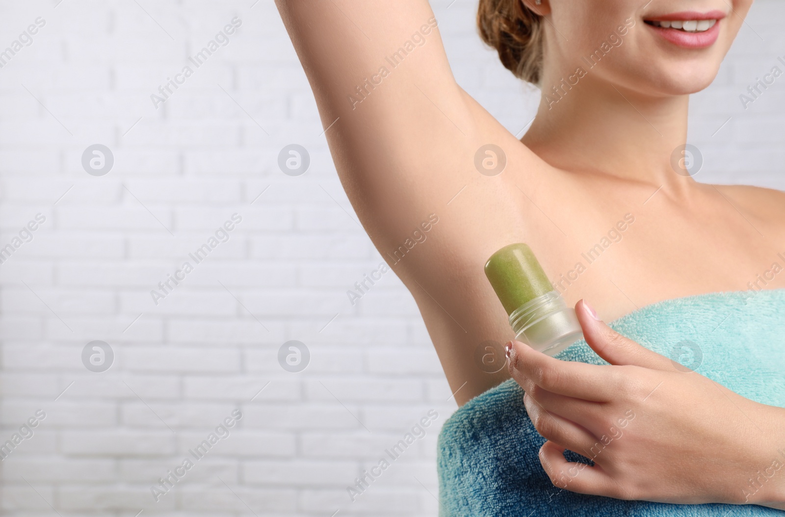 Photo of Young woman applying crystal alum deodorant to armpit against brick wall, closeup. Space for text