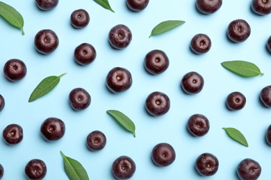 Photo of Fresh acai berries with leaves on blue background, flat lay