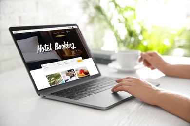 Woman using laptop to book hotel at white wooden table, closeup