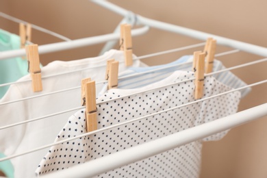 Photo of Different cute baby onesies hanging on clothes line against beige background, closeup. Laundry day