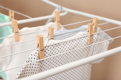 Different cute baby onesies hanging on clothes line against beige background, closeup. Laundry day