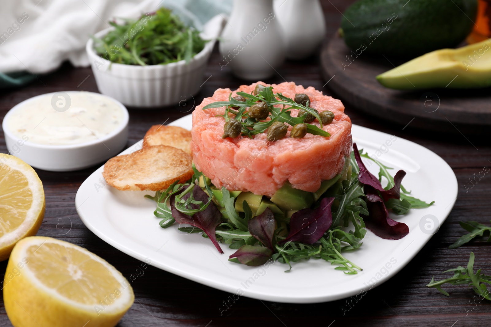 Photo of Tasty salmon tartare with avocado, greens and croutons on wooden table