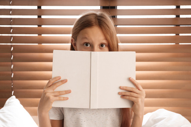 Emotional preteen girl with book on bed near window