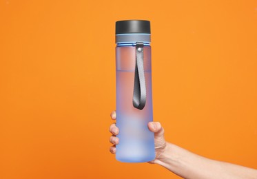 Woman holding bottle of water on orange background, closeup