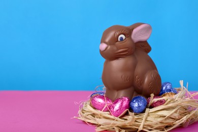 Chocolate Easter bunny and eggs on pink table against light blue background, closeup. Space for text
