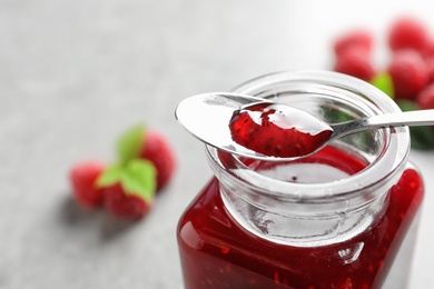 Glass jar and spoon of sweet raspberry jam on table, closeup. Space for text