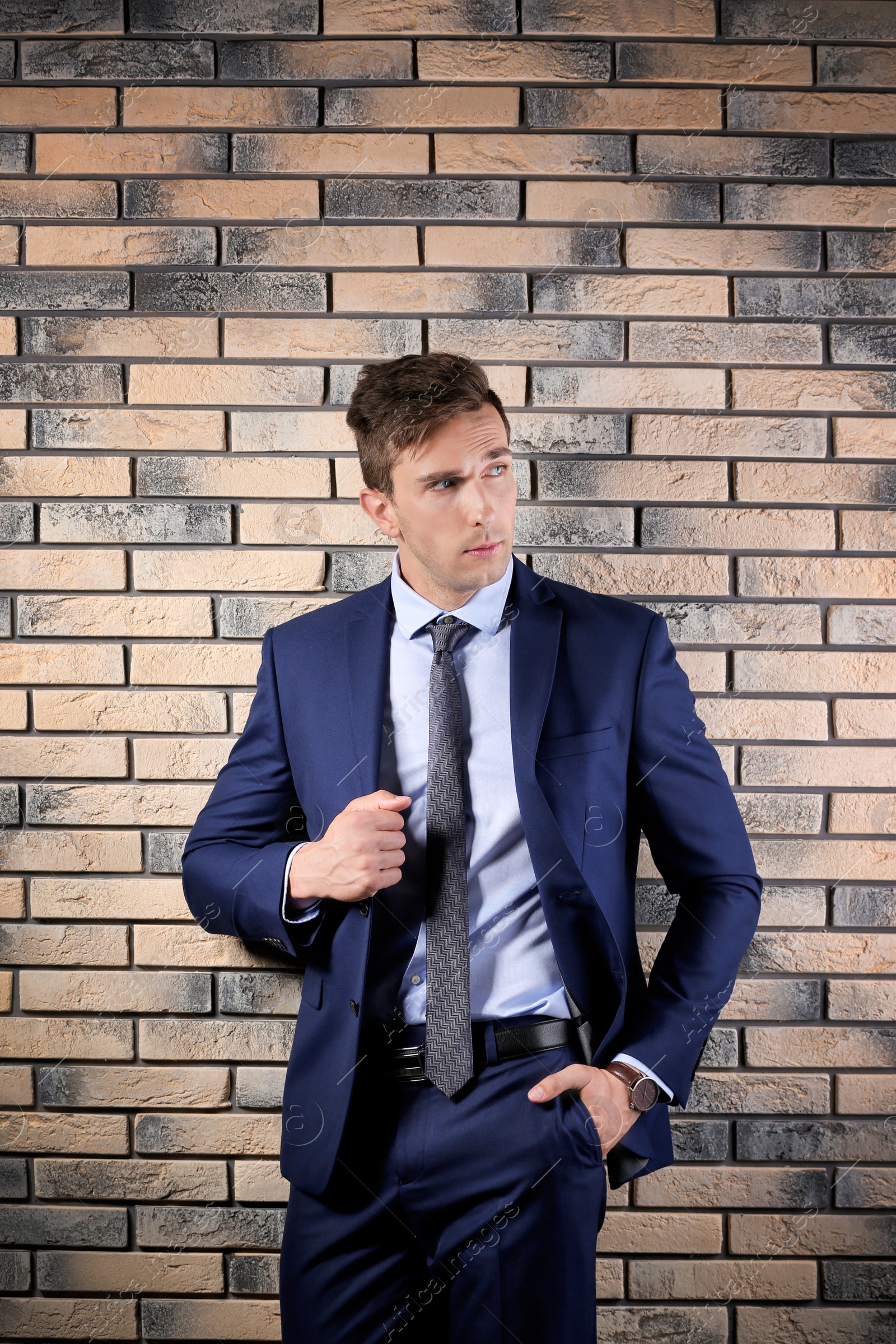 Photo of Handsome young man in suit near brick wall background