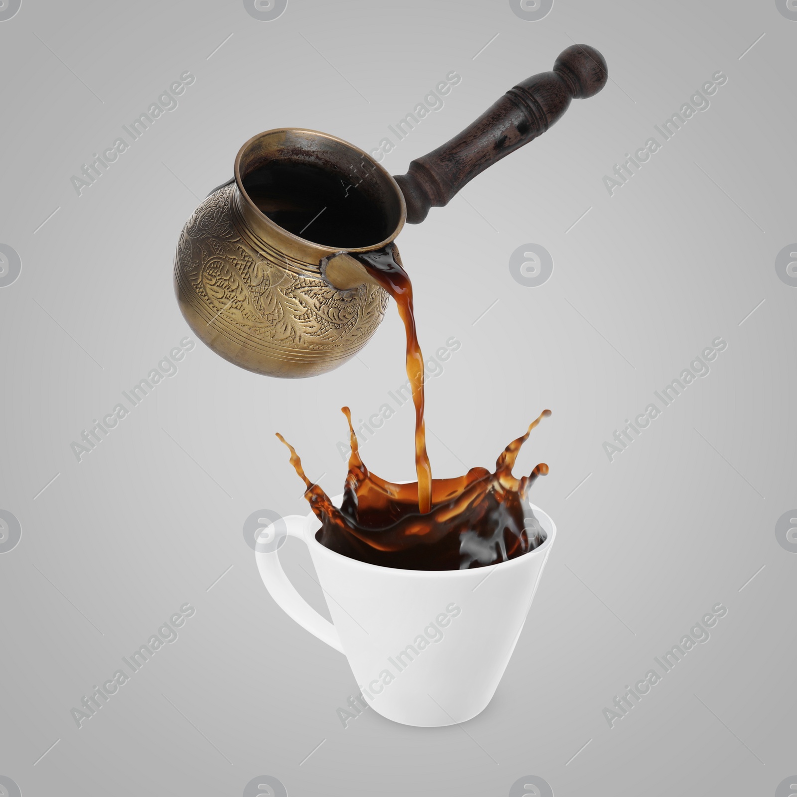 Image of Pouring freshly brewed aromatic coffee from turkish pot into cup. Objects in air on light grey background