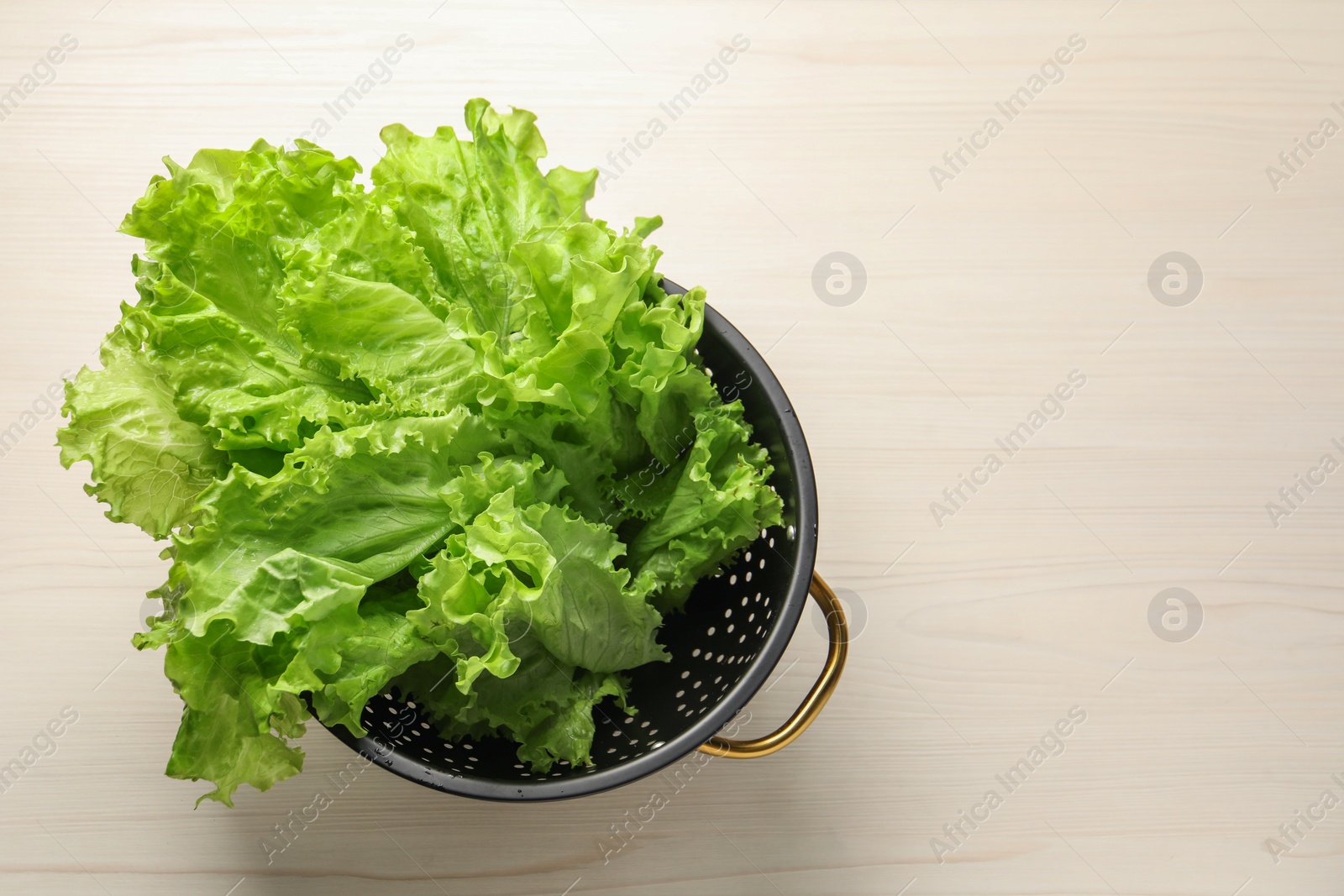 Photo of Fresh lettuce in black colander on white wooden table, top view. Space for text