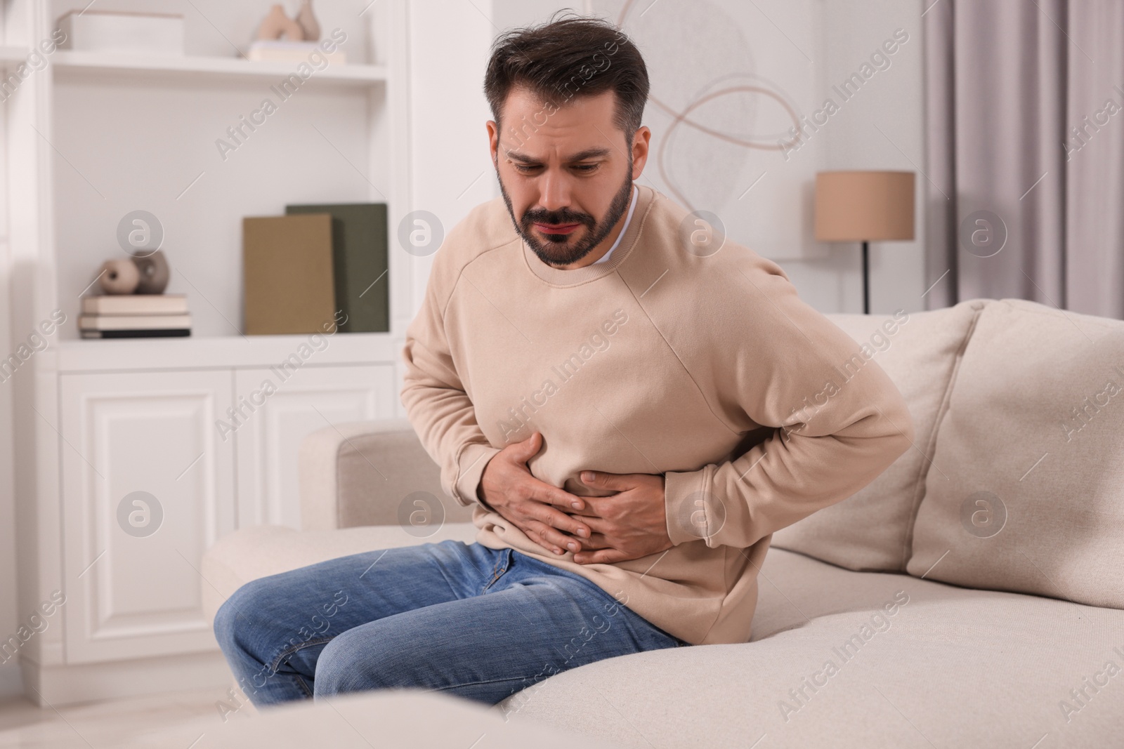 Photo of Unhappy man suffering from stomach pain on sofa at home
