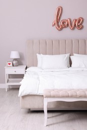 Photo of Cozy room interior with bed and balloon in shape of word Love. Valentine Day celebration