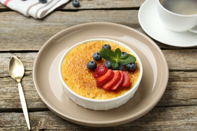 Photo of Delicious creme brulee with berries and mint in bowl on wooden table, closeup