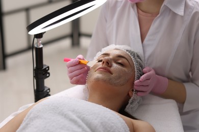 Photo of Cosmetologist applying mask on woman's face in clinic, closeup