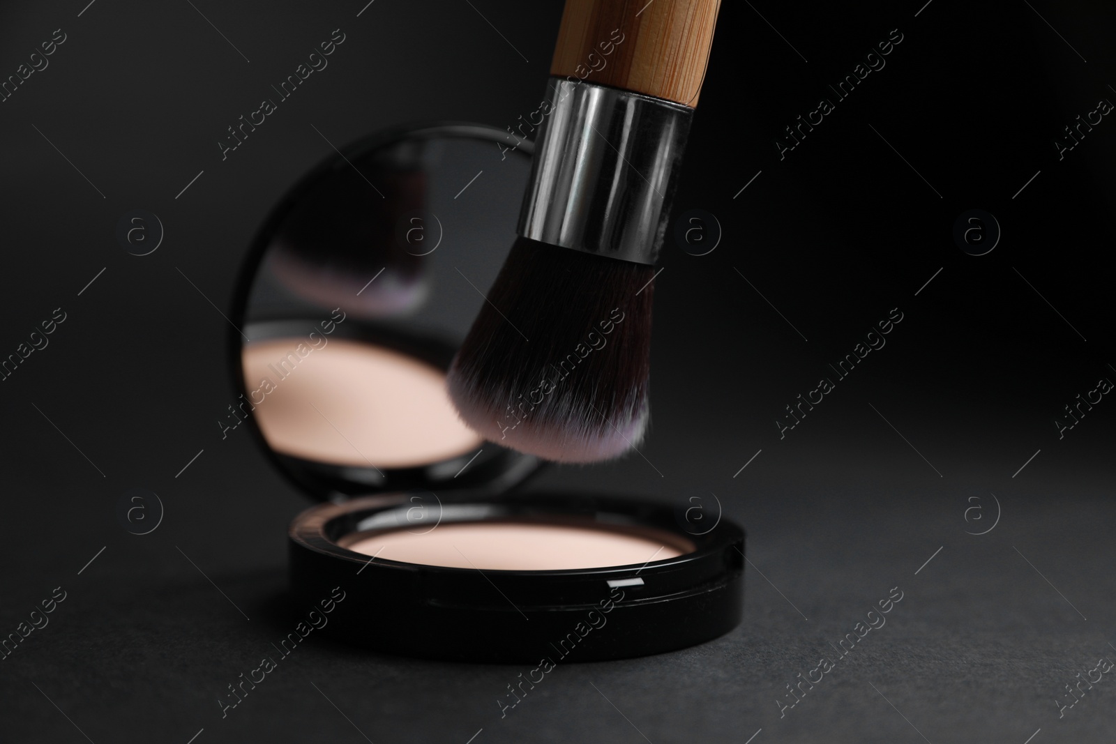 Photo of Makeup brush over face powder on black background, closeup