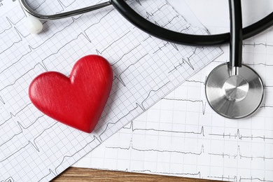 Photo of Cardiogram report, red decorative heart and stethoscope on wooden background, flat lay