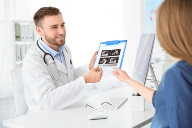 Photo of Gynecology consultation. Doctor showing ultrasound of baby to pregnant woman in clinic