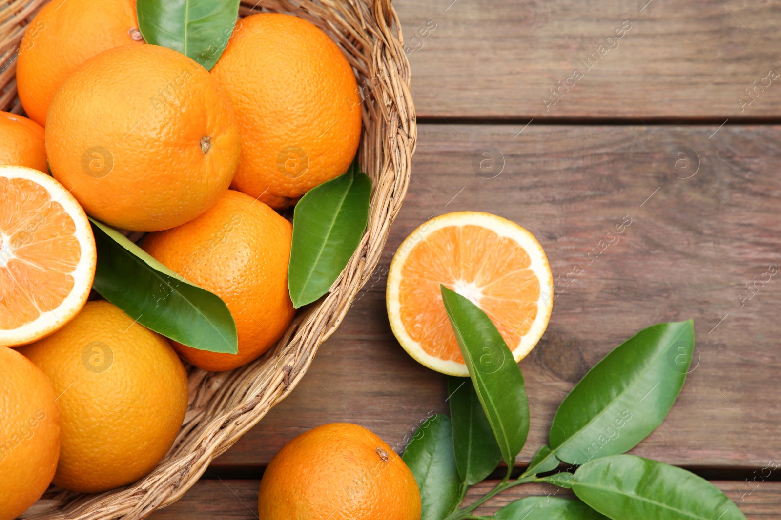 Photo of Wicker basket, ripe juicy oranges and green leaves on wooden table, flat lay