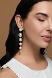 Photo of Young woman wearing elegant pearl earrings on brown background, closeup