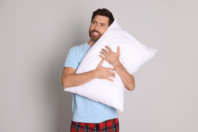 Photo of Smiling handsome man hugging soft pillow on light grey background