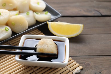 Taking raw scallop from bowl of soy sauce with chopsticks at wooden table, closeup. Space for text