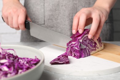 Photo of Woman cutting fresh red cabbage at light grey table, closeup