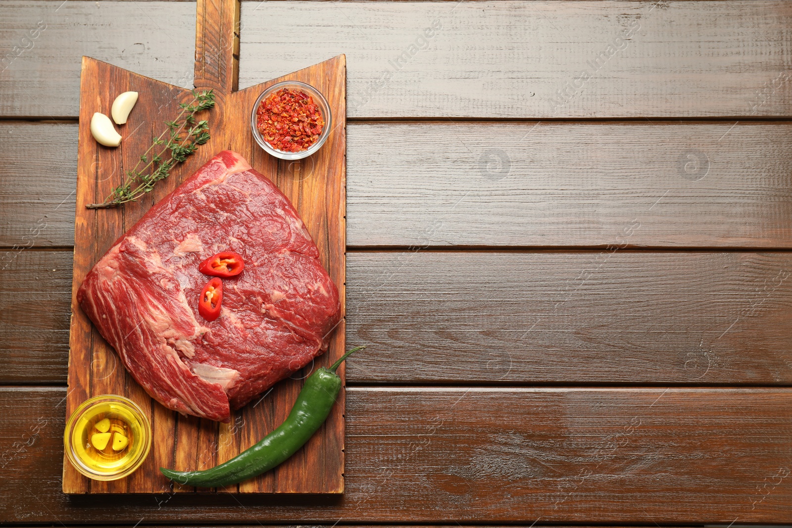 Photo of Fresh raw beef cut, spices and oil on wooden table, top view. Space for text