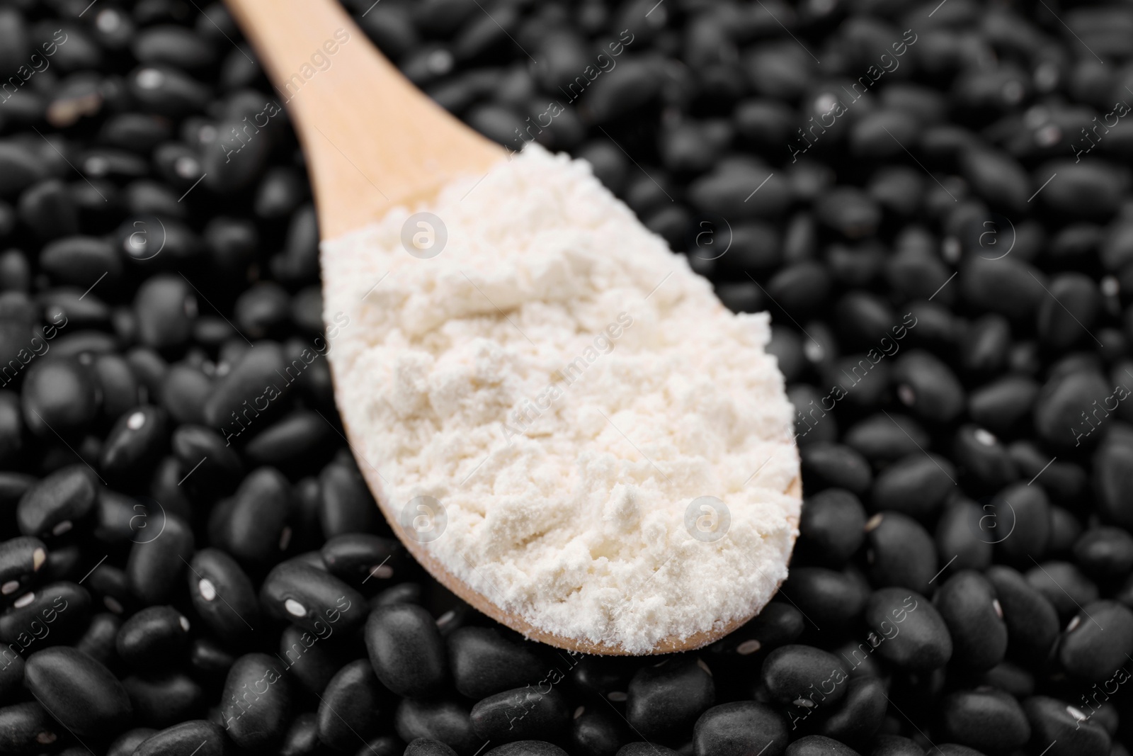 Wooden spoon with flour on black kidney beans, closeup Photo of Wooden spoon with flour on black kidney beans, closeup