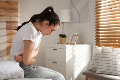 Photo of Young woman suffering from stomach ache on bed at home, space for text. Food poisoning