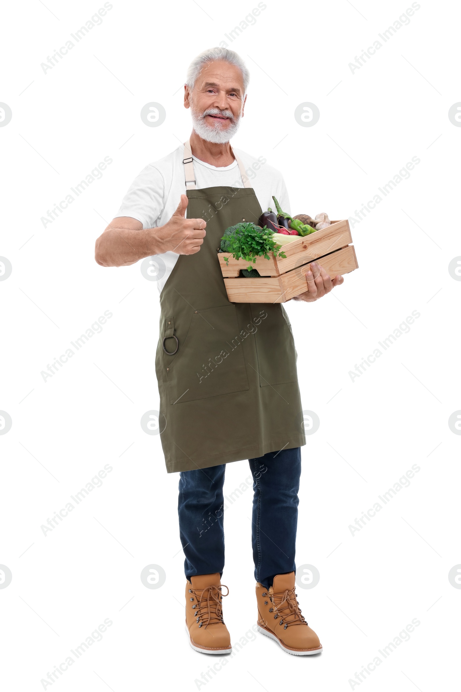 Photo of Harvesting season. Happy farmer holding wooden crate with vegetables and showing thumb up on white background