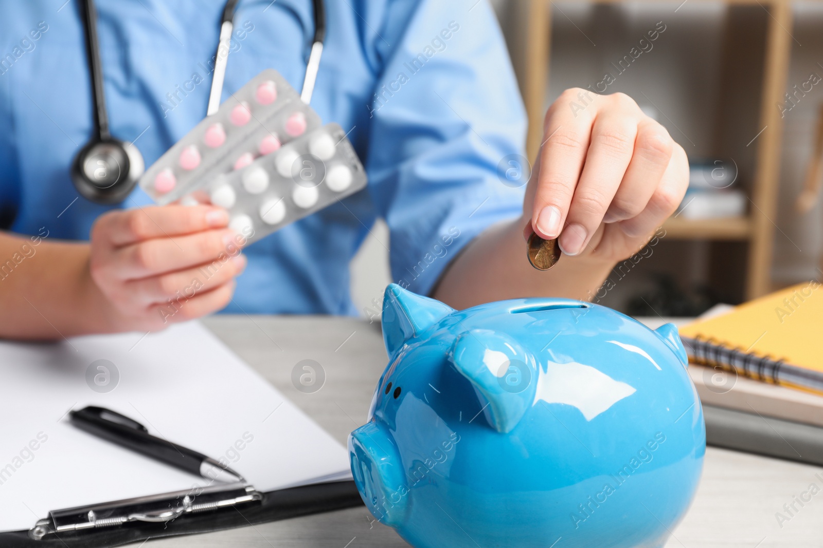 Photo of Doctor putting coin into piggy bank and holding pills at wooden table in hospital, closeup. Medical insurance