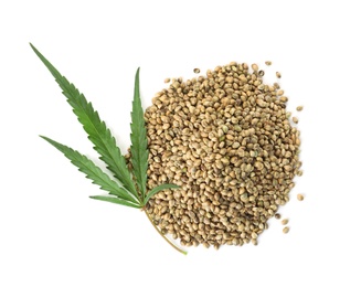 Pile of hemp seeds with green leaf on white background, top view