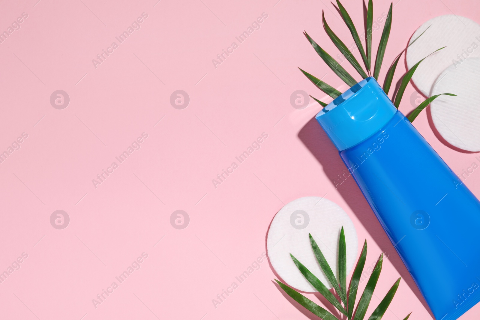 Photo of Tube of face cleansing product, leaves and cotton pads on pink background, flat lay. Space for text