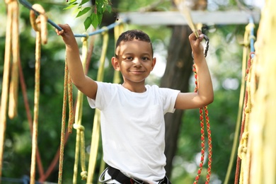 Little African-American boy climbing in adventure park. Summer camp