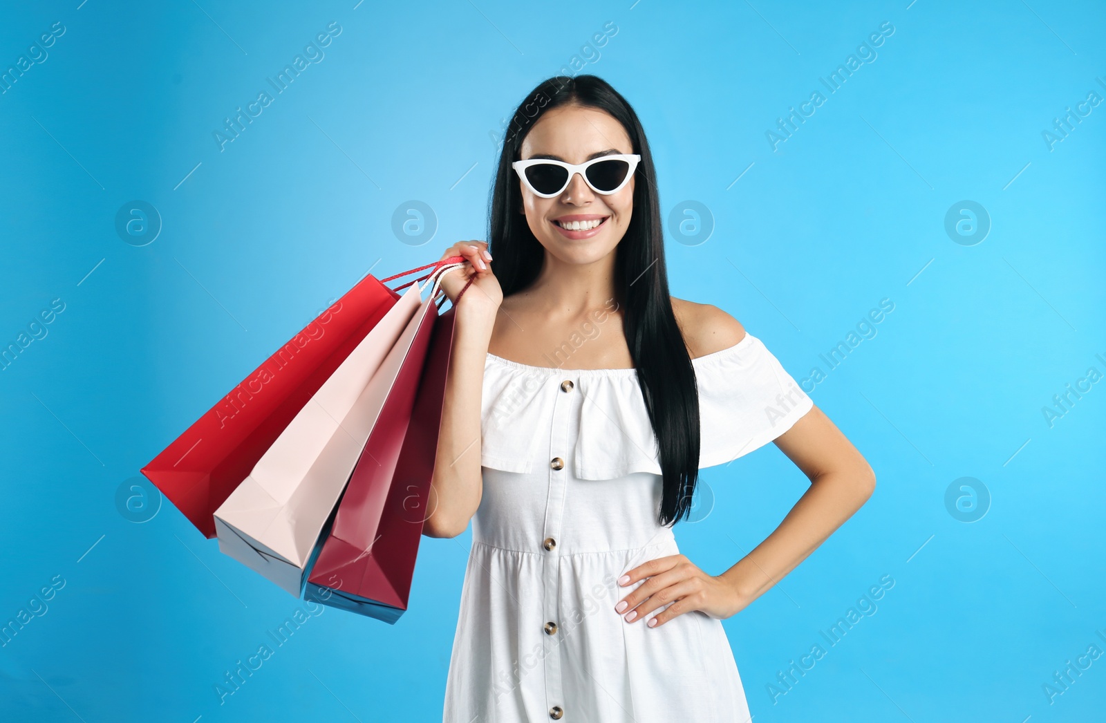 Photo of Beautiful young woman with paper shopping bags on light blue background