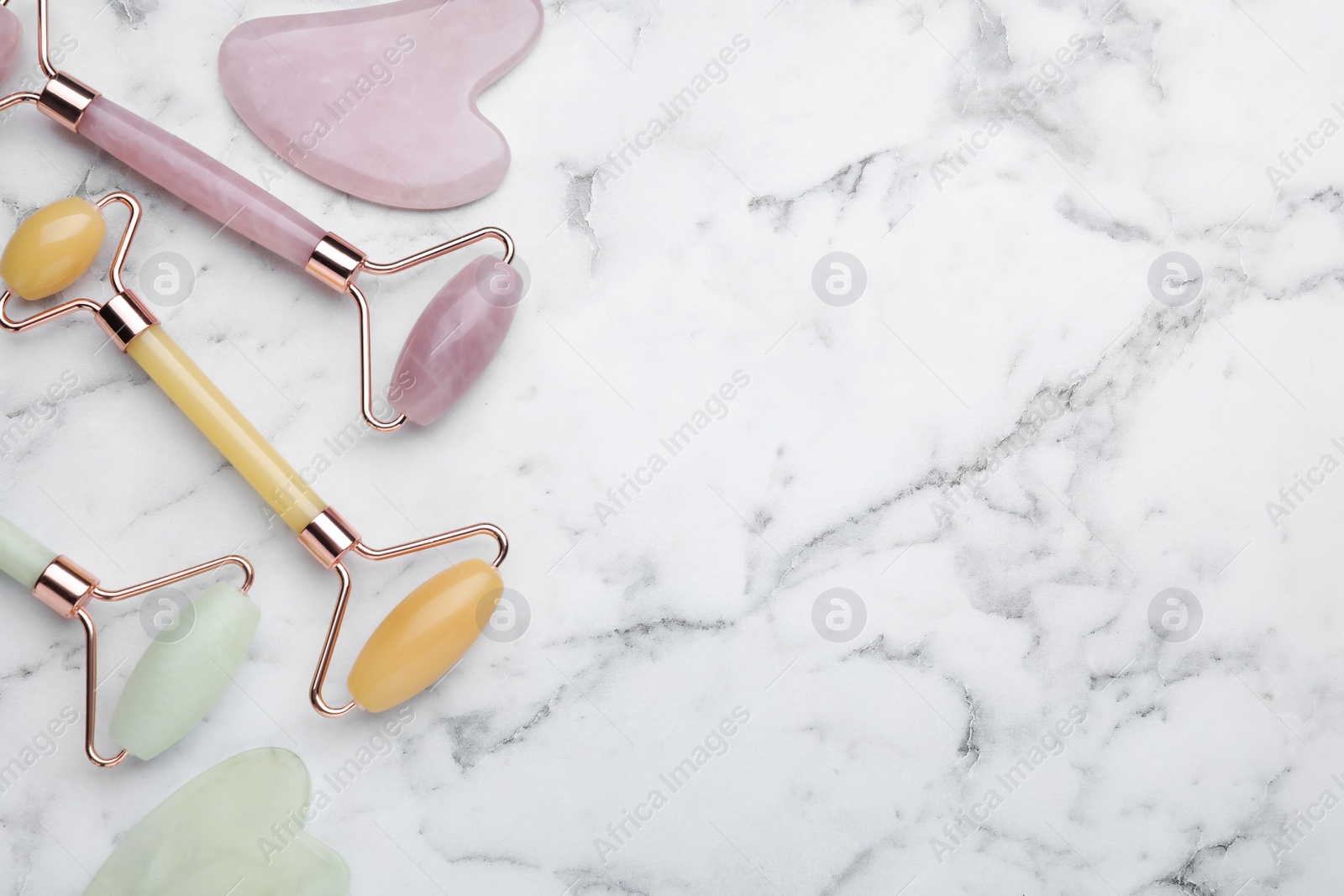 Photo of Different gua sha stones and face rollers on white marble table, flat lay. Space for text