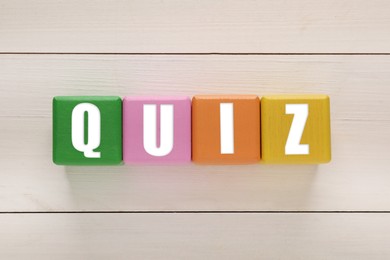 Photo of Colorful cubes with word Quiz on white wooden table, flat lay