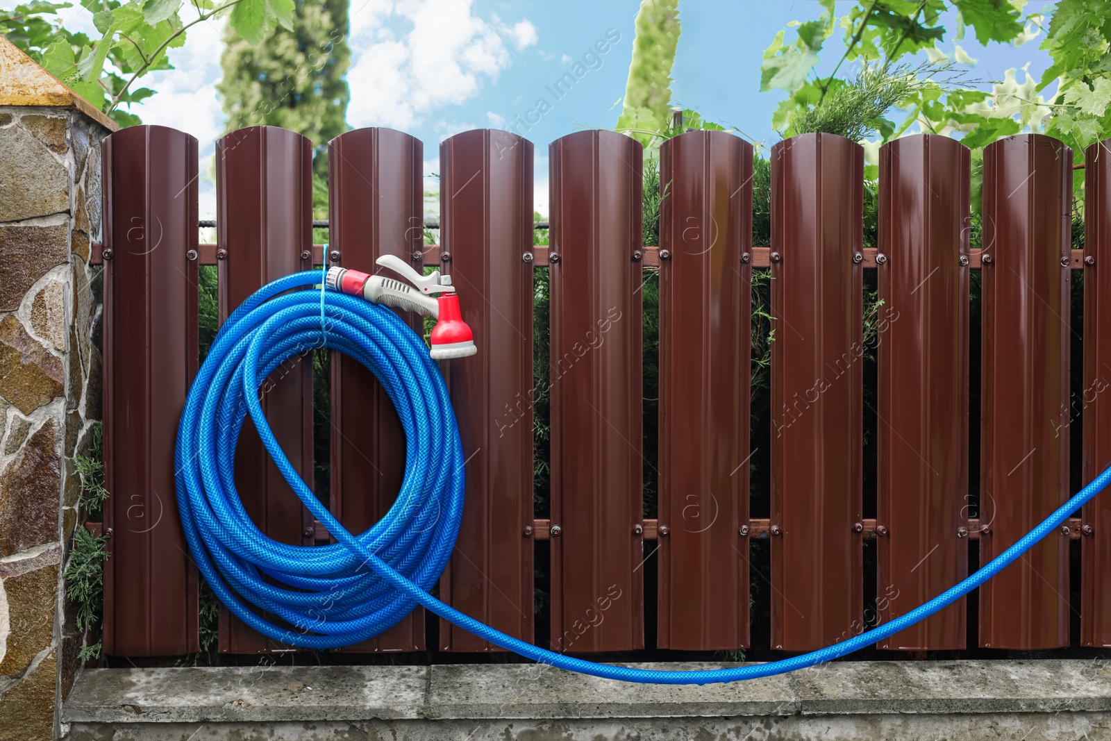 Photo of Watering hose with sprinkler hanging on wooden fence in garden