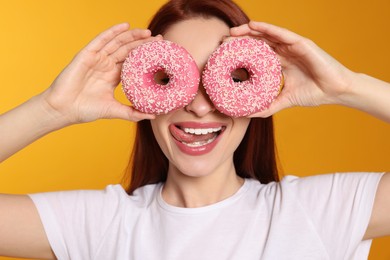 Photo of Beautiful redhead woman covering eyes with donut on orange background