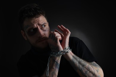Photo of Scared man with bruise chained on dark background. Hostage