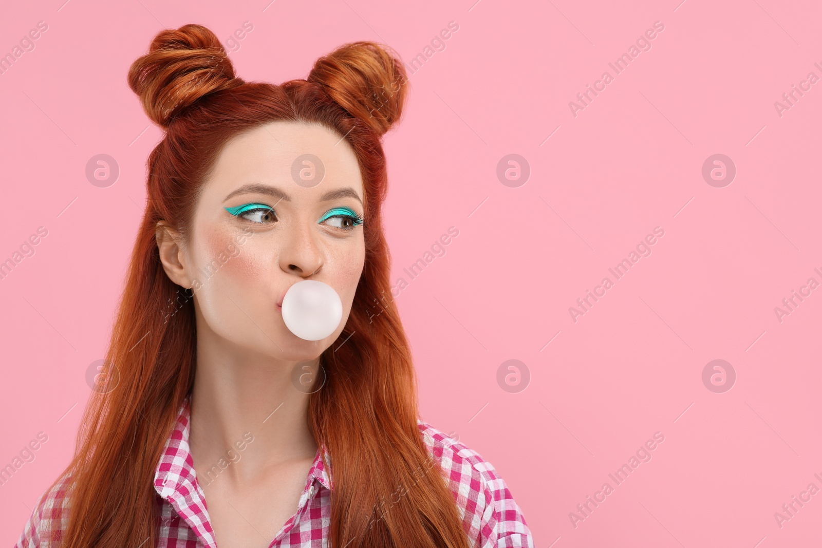 Photo of Beautiful woman with bright makeup blowing bubble gum on pink background. Space for text