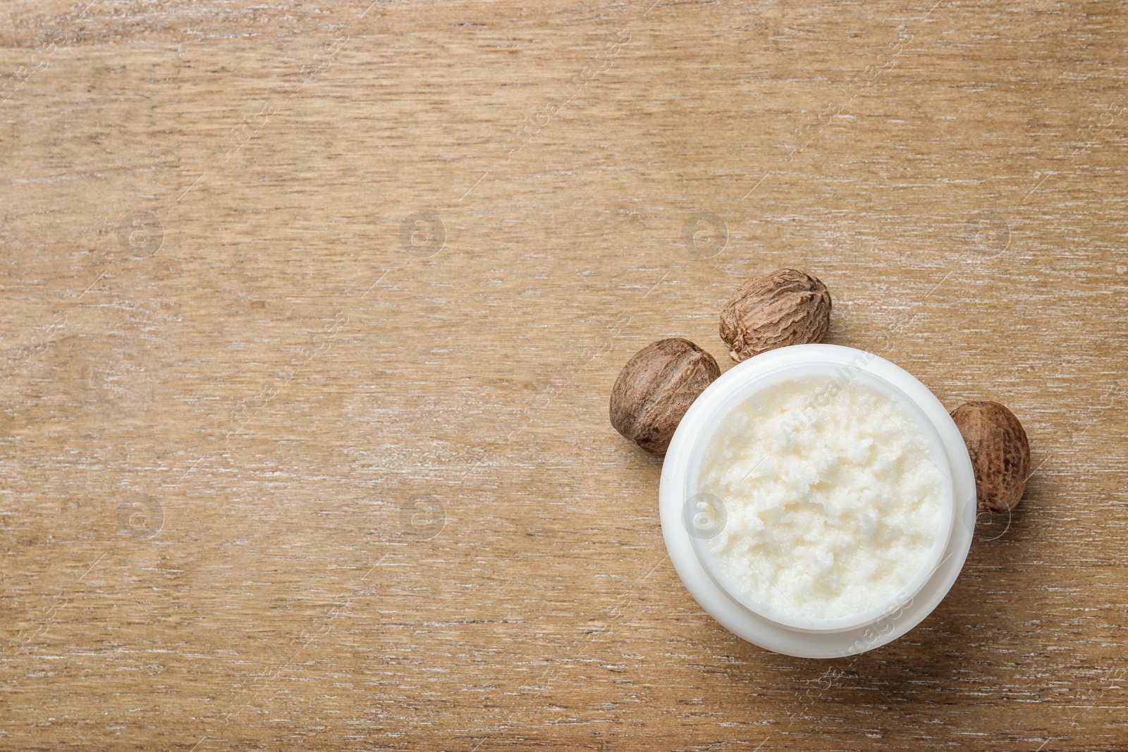 Photo of Jar of shea butter, nuts and space for text on wooden background, top view