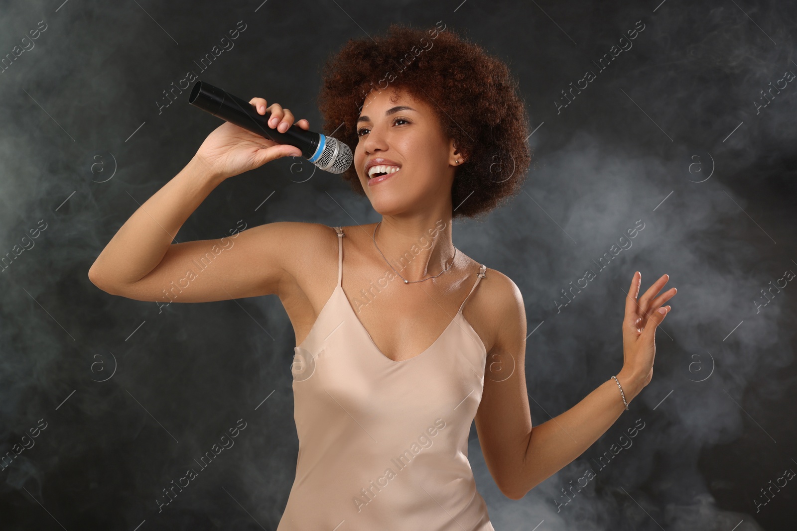 Photo of Curly young woman with microphone singing in smoke on black background