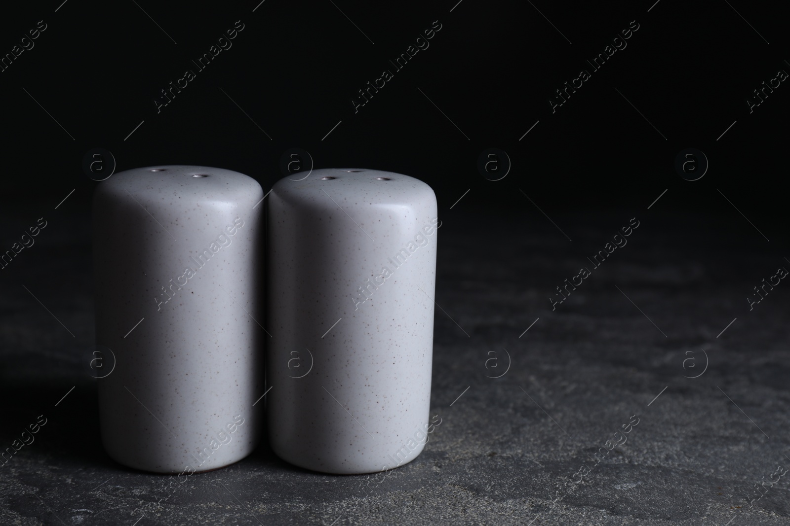 Photo of Salt and pepper shakers on dark textured table. Space for text