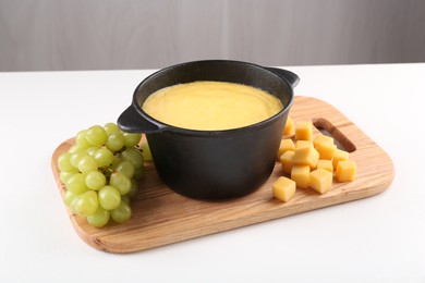 Photo of Fondue with tasty melted cheese and grapes on white table