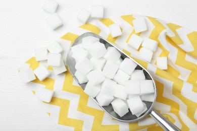 Many sugar cubes and metal scoop on white wooden table, top view