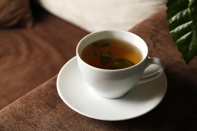 Photo of Cup of tasty herbal tea on sofa, closeup