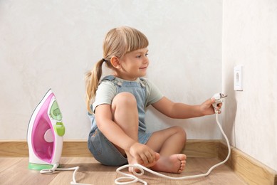 Photo of Little child playing with electrical socket and iron plug at home. Dangerous situation