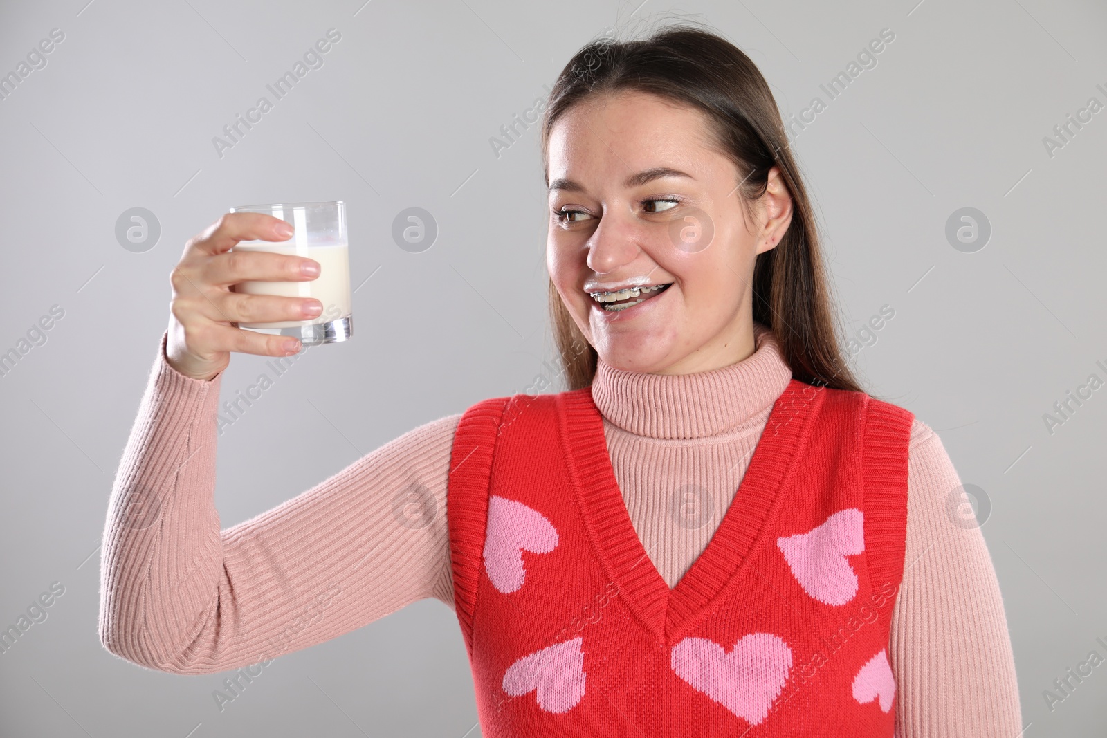 Photo of Happy woman with milk mustache holding glass of drink on light grey background