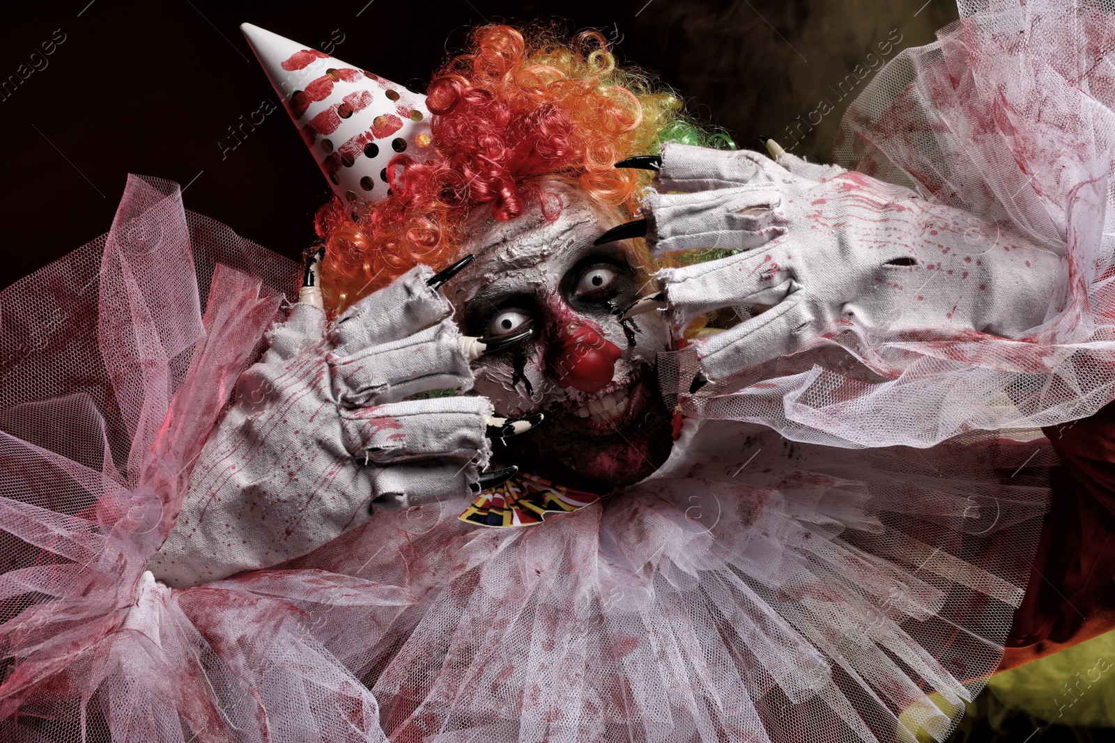 Photo of Terrifying clown on dark background. Halloween party costume