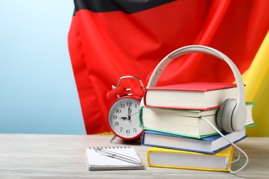 Photo of Learning foreign language. Different books, headphones, alarm clock and stationery on wooden table near flag of Germany, space for text